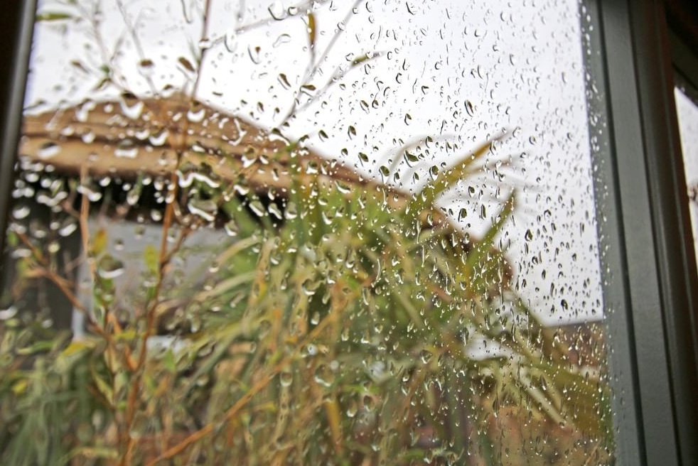 Rain on window on garden studio with view on breeze house thatched roof