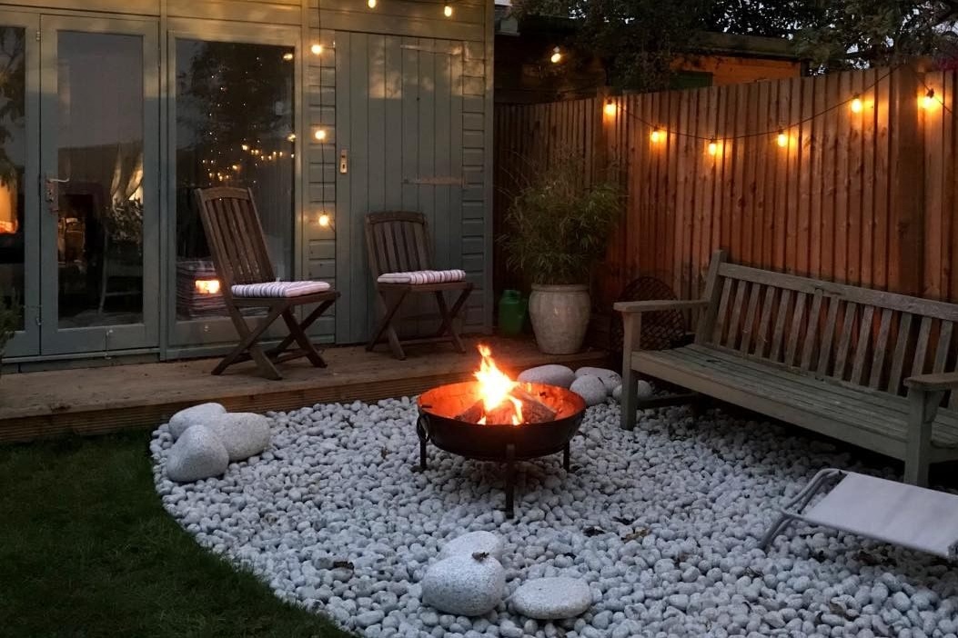 Early evening in garden with lit firepit and festoon lights decorating garden studio