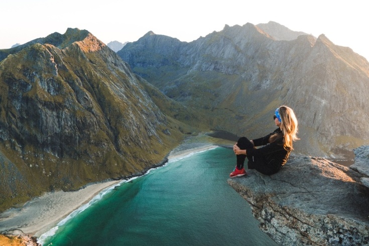 View of stunning landscape in Norway with girl sat on cliff edge overlooking Fjord