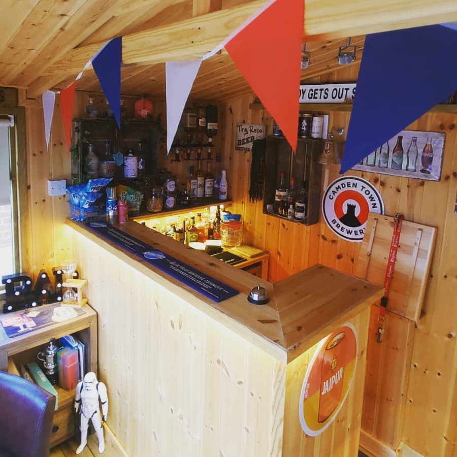 The interior of a wooden garden building that has a wooden bar stocked with beers and spirits.