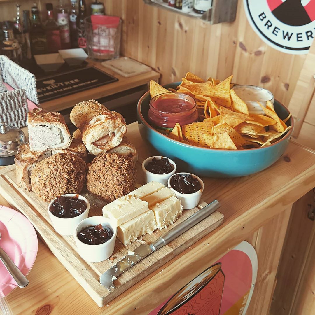 A food platter of pastries, scotch eggs, cheese, chutney, crisps and dips