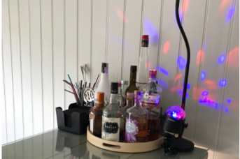 A collection of alcoholic spirits sit atop a bar, next to multicoloured disco lights that dance up the wall