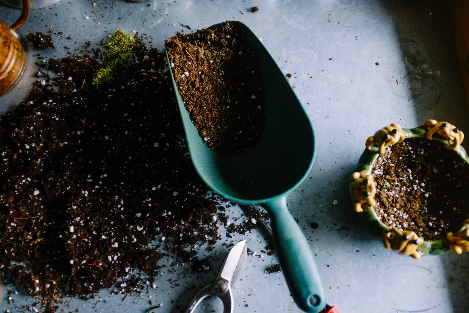 An arial view of a trowel lying on a concrete surface, surrounded by a soil mixture with stony flecks. Be inspired to grow your own in a victory garden at home.