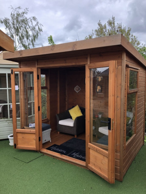 A small, square redwood summerhouse with large windows and double doors. The doors are open to show the interior.