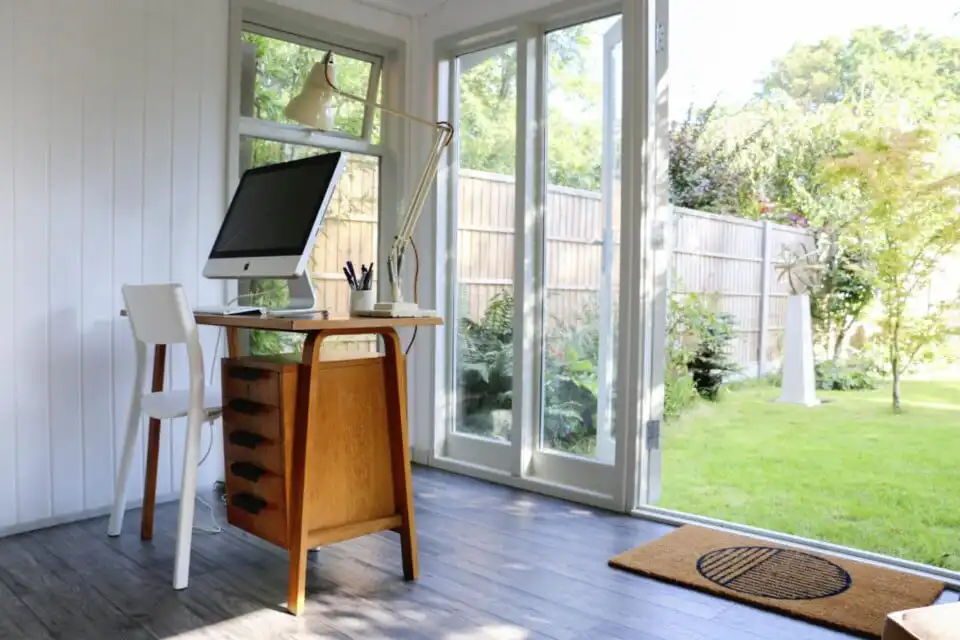 Desk with desktop PC and drawing equipment, inside of a Garden Office with large open sliding doors out onto the garden space.