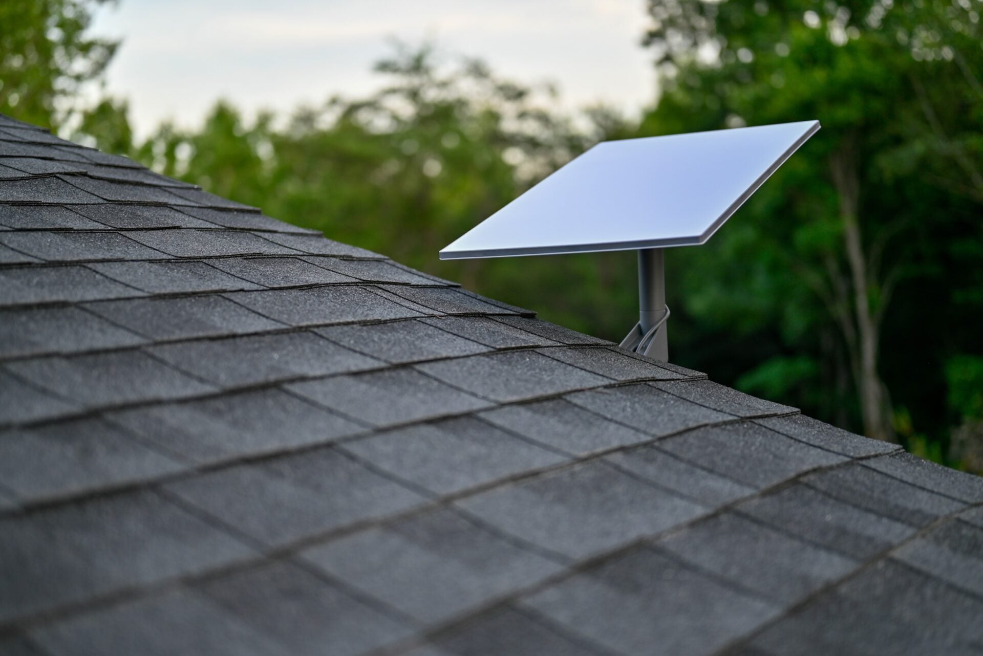Starlink satellite dish with a wall mount on a shingle roof.