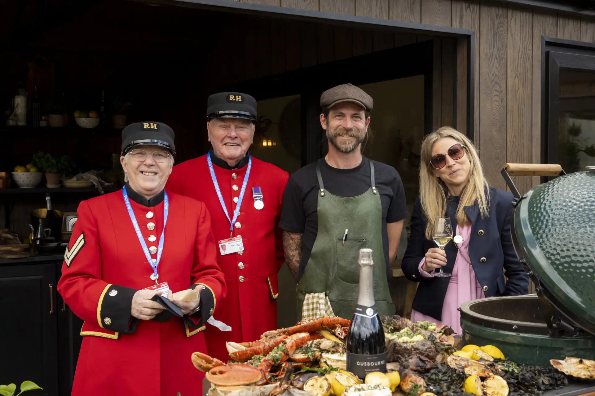 Chef James Strawbridge with Chelsea Pensioners and a show visitor on the Malvern Garden Buildings tradestand at Chelsea Flower Show 2026